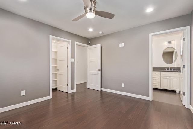 unfurnished bedroom with a spacious closet, dark wood-style flooring, a sink, and baseboards