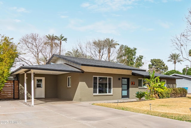 single story home with brick siding, board and batten siding, a front yard, an attached carport, and driveway