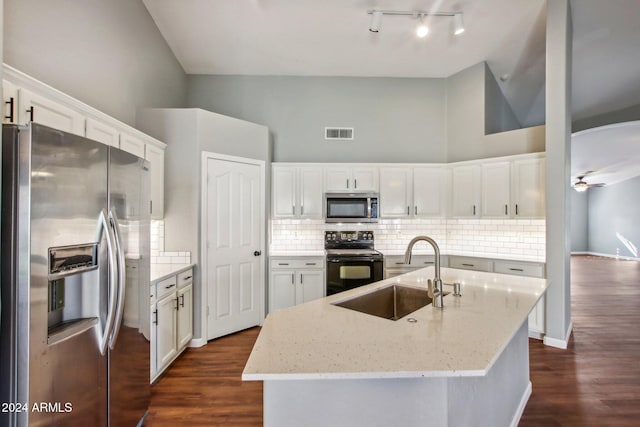 kitchen featuring a towering ceiling, stainless steel appliances, a kitchen island with sink, sink, and white cabinetry