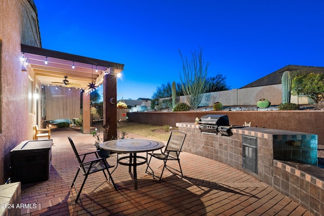 patio terrace at dusk with area for grilling, ceiling fan, and a grill