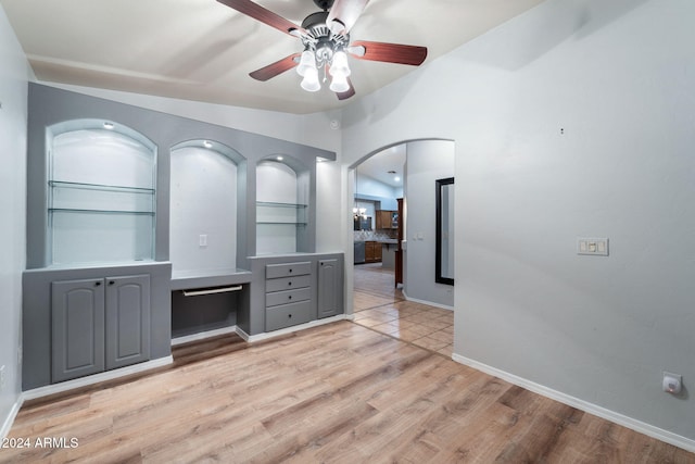 interior space featuring built in shelves, ceiling fan, vaulted ceiling, and light wood-type flooring