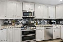 kitchen with white cabinets, light stone countertops, tasteful backsplash, and stainless steel appliances