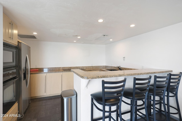 kitchen featuring black appliances, light stone counters, kitchen peninsula, a kitchen bar, and dark hardwood / wood-style flooring