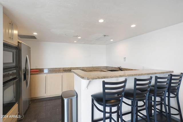 kitchen with visible vents, black appliances, light stone counters, a breakfast bar area, and dark wood-style floors