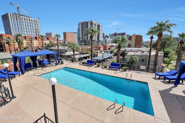 pool with a gazebo, a city view, a patio, and fence