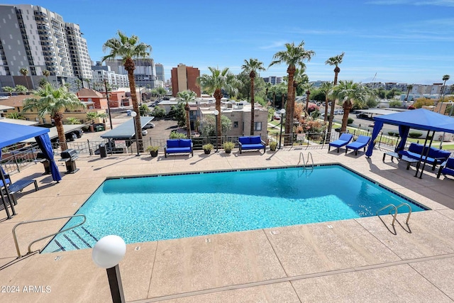 community pool with a patio area, fence, and a city view