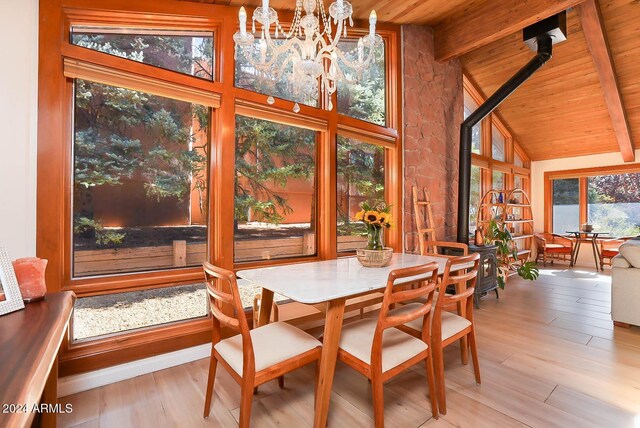 dining room featuring a wood stove, lofted ceiling with beams, light hardwood / wood-style flooring, a notable chandelier, and wood ceiling