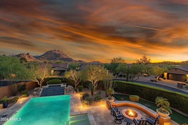 pool at dusk featuring an outdoor fire pit, a patio area, and a mountain view