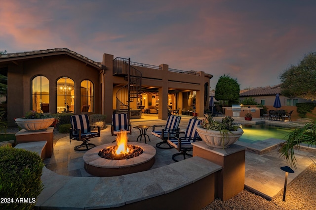 back house at dusk with a balcony, an outdoor fire pit, and a patio