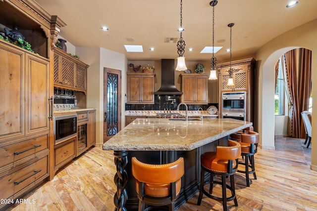 kitchen with a skylight, a kitchen bar, light wood-type flooring, backsplash, and custom exhaust hood