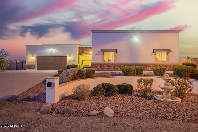 view of front of property featuring a garage, stone siding, fence, and stucco siding