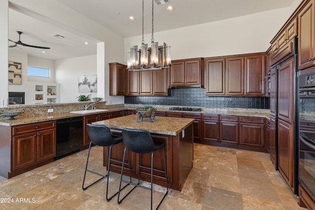 kitchen featuring light stone countertops, sink, black appliances, backsplash, and a center island