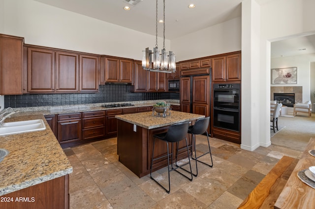 kitchen with sink, black appliances, a center island, decorative light fixtures, and a towering ceiling