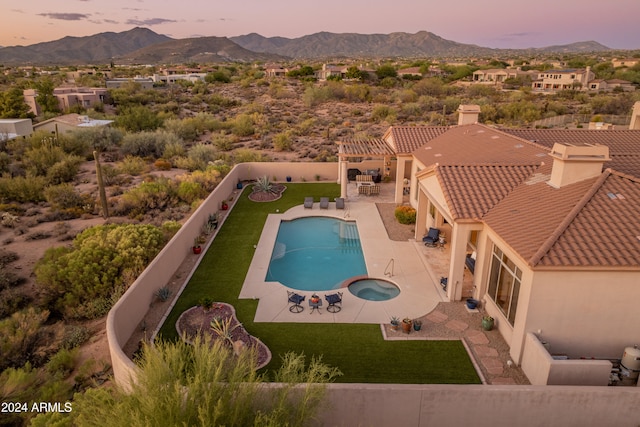 pool at dusk featuring a patio, a mountain view, an in ground hot tub, and a lawn