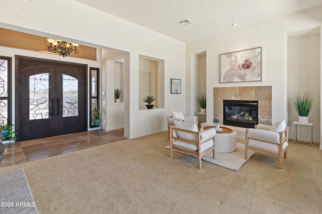 carpeted entryway featuring french doors, a tiled fireplace, and a notable chandelier