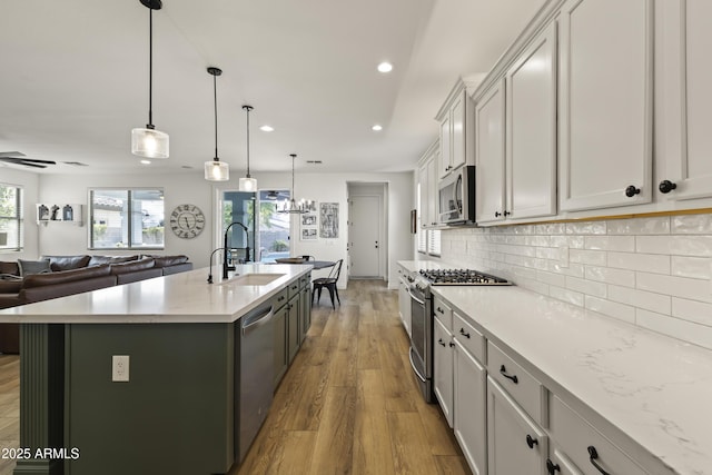 kitchen with stainless steel appliances, tasteful backsplash, open floor plan, a sink, and wood finished floors