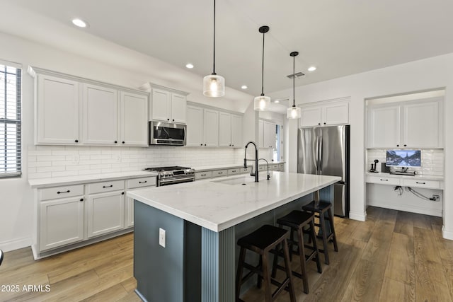 kitchen featuring a breakfast bar, stainless steel appliances, visible vents, a sink, and wood finished floors