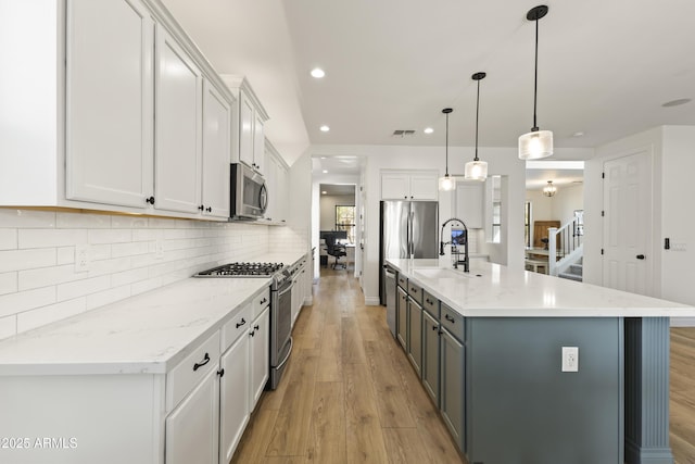 kitchen featuring light wood finished floors, white cabinets, decorative backsplash, appliances with stainless steel finishes, and a sink