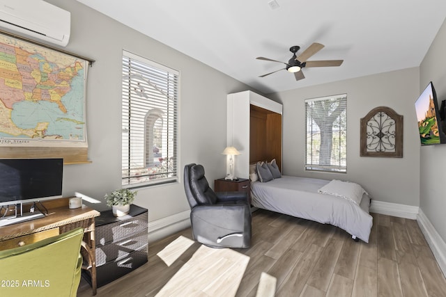 bedroom featuring a wall mounted AC, wood finished floors, a ceiling fan, and baseboards