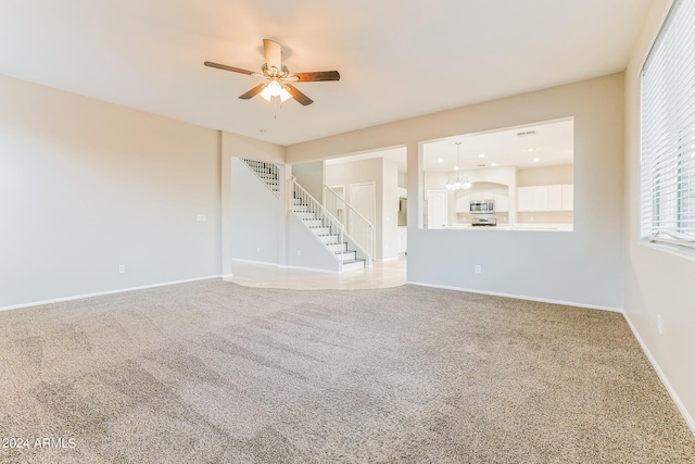 unfurnished living room featuring carpet and ceiling fan with notable chandelier