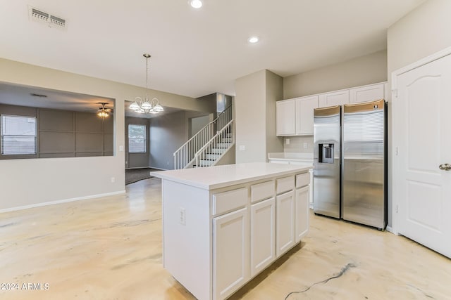 kitchen featuring hanging light fixtures, stainless steel fridge, a center island, white cabinetry, and ceiling fan with notable chandelier