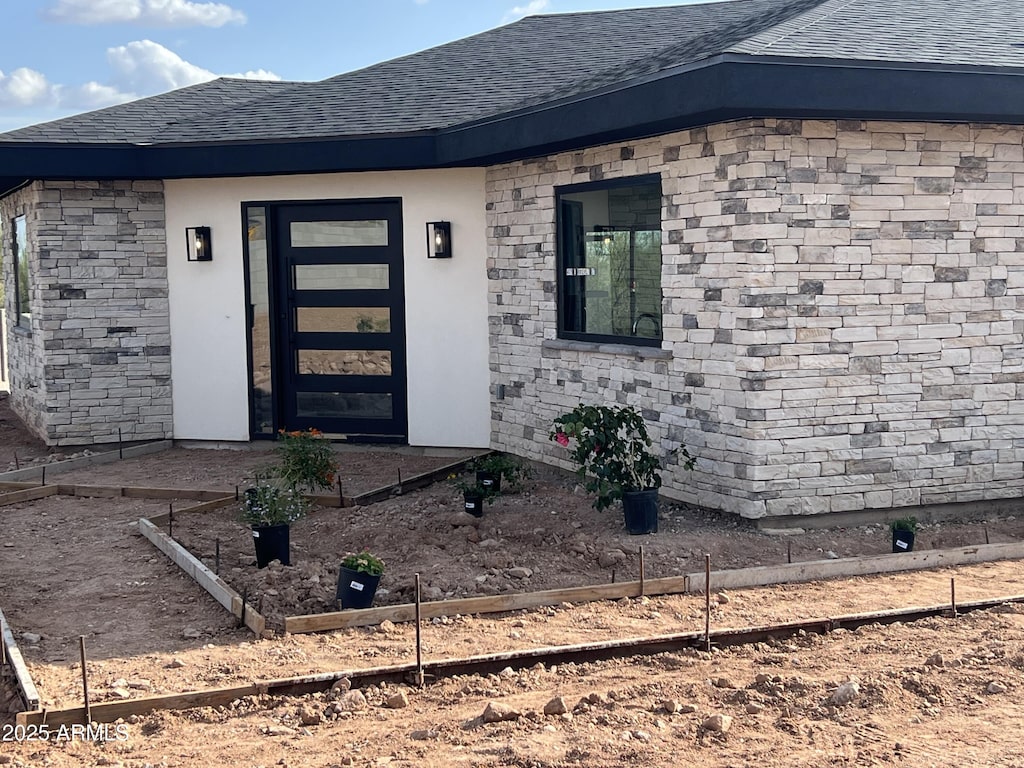 doorway to property with a shingled roof and stone siding