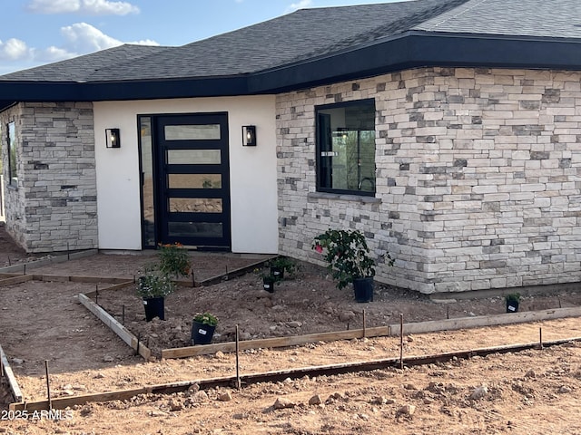 doorway to property with a shingled roof and stone siding