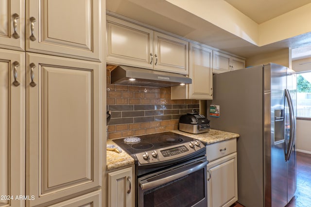 kitchen with light stone countertops, tasteful backsplash, dark hardwood / wood-style flooring, appliances with stainless steel finishes, and cream cabinetry