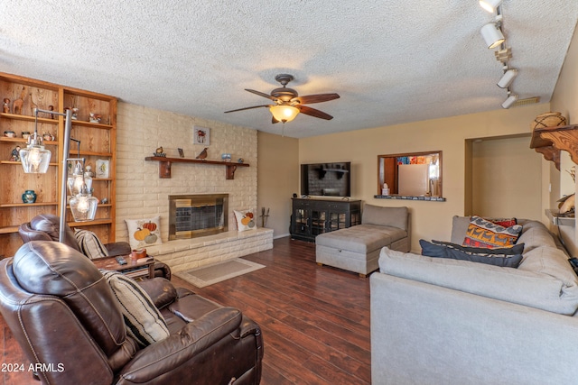 living room with ceiling fan, a brick fireplace, a textured ceiling, rail lighting, and dark hardwood / wood-style flooring