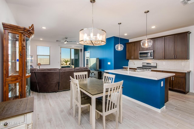 kitchen with ceiling fan, hanging light fixtures, backsplash, a center island with sink, and appliances with stainless steel finishes