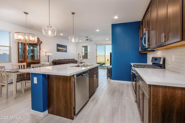 kitchen with appliances with stainless steel finishes, ceiling fan with notable chandelier, sink, hanging light fixtures, and an island with sink