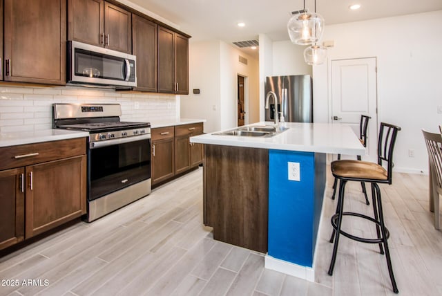 kitchen with sink, hanging light fixtures, stainless steel appliances, backsplash, and a center island with sink