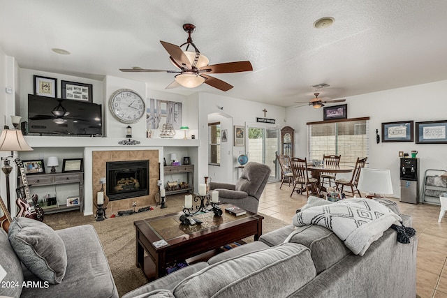 living room featuring tile floors, ceiling fan, a textured ceiling, and a fireplace