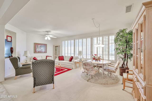 living area featuring ceiling fan with notable chandelier, visible vents, and light colored carpet