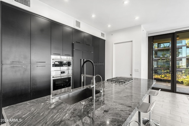 kitchen with sink, expansive windows, dark stone countertops, a kitchen bar, and appliances with stainless steel finishes