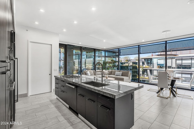 kitchen featuring a wealth of natural light, floor to ceiling windows, stainless steel gas cooktop, sink, and a center island with sink