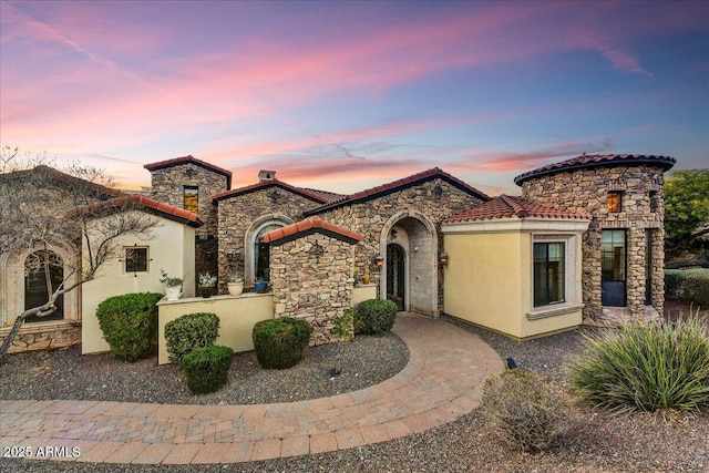 mediterranean / spanish home with a tiled roof, stone siding, and stucco siding