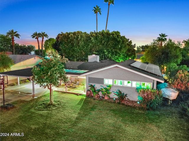 back house at dusk featuring a yard, a patio, solar panels, and a carport