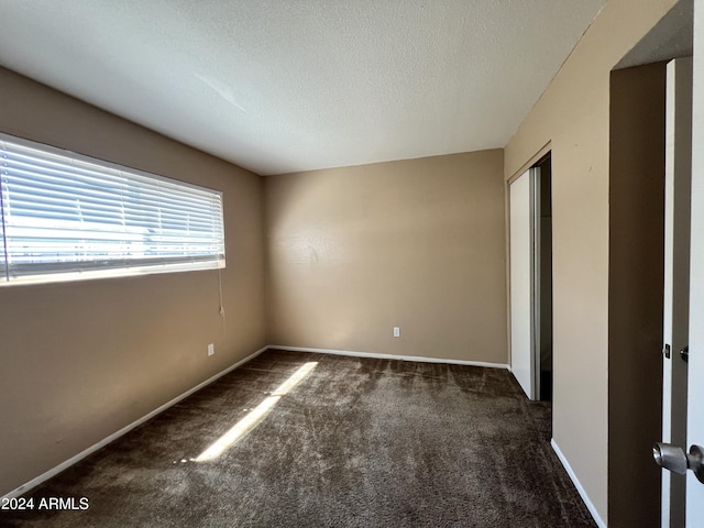 unfurnished room featuring a textured ceiling and dark colored carpet