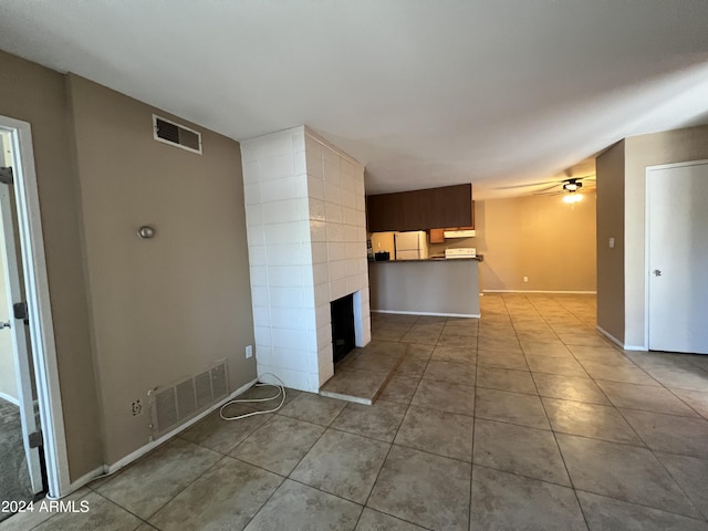 unfurnished living room featuring a tiled fireplace, light tile patterned floors, and ceiling fan