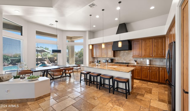 kitchen with a center island with sink, a healthy amount of sunlight, decorative light fixtures, and ventilation hood