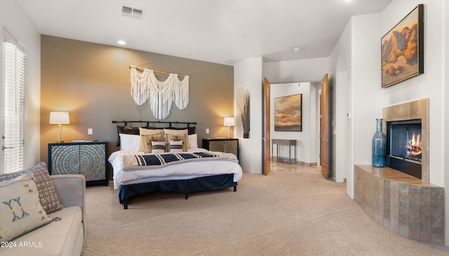 bedroom featuring light colored carpet and a tiled fireplace