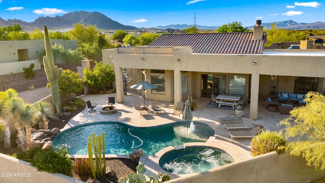 exterior space with a mountain view, a swimming pool with hot tub, a fire pit, and a patio area