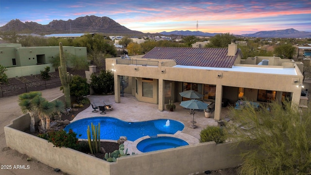 pool at dusk with a mountain view, an in ground hot tub, and a patio area