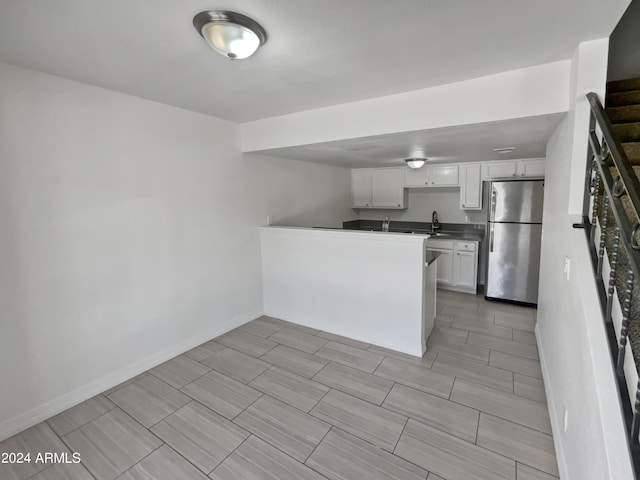 kitchen featuring stainless steel fridge, white cabinetry, and sink