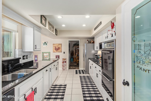 kitchen featuring backsplash, light tile patterned floors, white cabinetry, stainless steel refrigerator, and sink