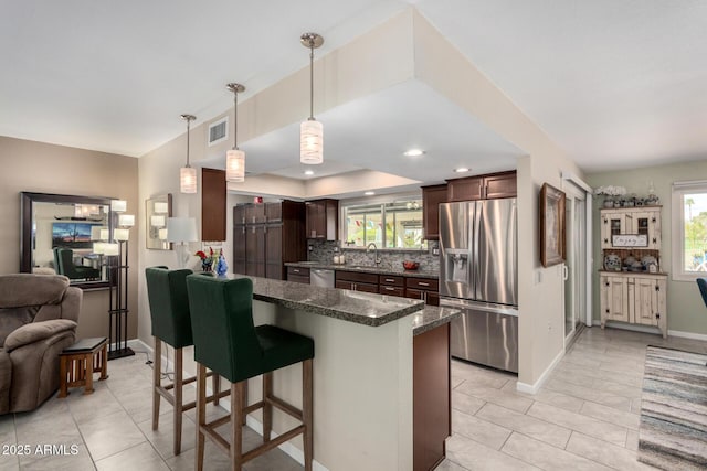 kitchen featuring visible vents, backsplash, stainless steel appliances, dark brown cabinetry, and a breakfast bar area