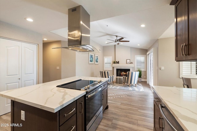 kitchen with island exhaust hood, appliances with stainless steel finishes, light stone counters, and lofted ceiling