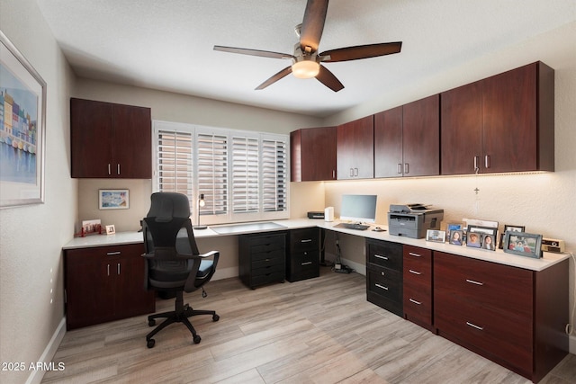 home office featuring ceiling fan, built in desk, and light hardwood / wood-style flooring