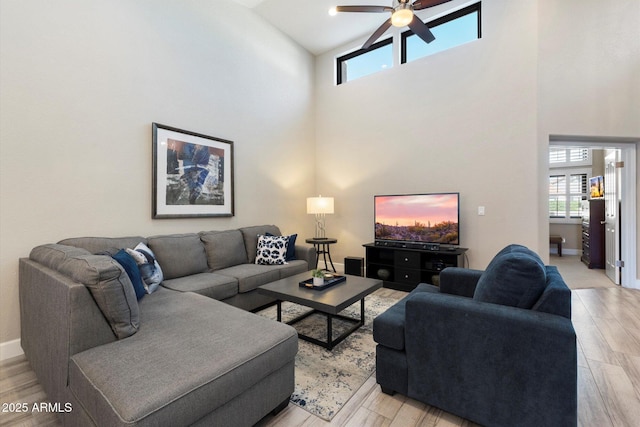 living room with ceiling fan, light hardwood / wood-style floors, and a towering ceiling